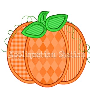 May include: An orange pumpkin applique with a green stem and leaves. The pumpkin is made of three different fabrics: a checkered pattern, a diamond pattern, and a striped pattern. The text "Appliquation Station" is visible on the pumpkin.