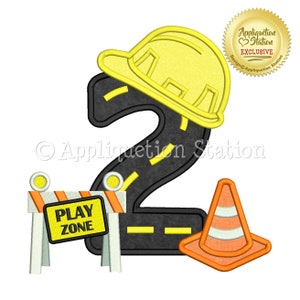 May include: A yellow construction hat sits on top of a black number two shaped like a road. A yellow and orange construction barricade with the words "PLAY ZONE" is on the left side of the number. A yellow and orange traffic cone is on the right side of the number.