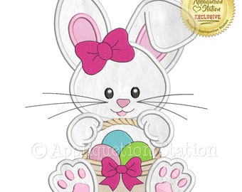 May include: A white bunny with pink ears and a pink bow holds a basket of colorful Easter eggs. The bunny is sitting on its bottom with its paws out in front of it. The basket is brown with a pink bow.