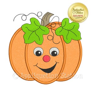 May include: An orange pumpkin with a smiling face, green leaves, and a brown stem. The pumpkin has a red nose, black eyes, and a curved black mouth. The text "Appliquetion Station" is at the bottom, and a gold seal says "Appliquetion Station EXCLUSIVE".