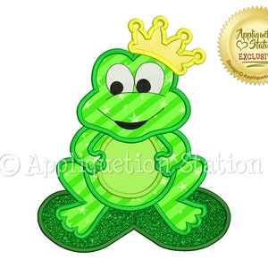Może przedstawiać: Zielona żaba w złotej koronie, siedząca na zielonym liściu. Żaba ma pasiasty wzór i szeroki uśmiech. Obrazek jest do haftu.