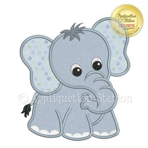 May include: A light blue cartoon elephant with large eyes and a small tuft of hair. The elephant has patterned ears with green and blue polka dots. The image includes the text "Appliquation Station EXCLUSIVE".