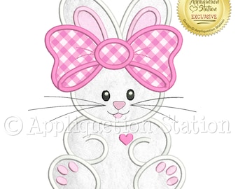 May include: White bunny with pink gingham bow and a pink heart on its chest. The bunny is sitting with its paws in front of it. The image is a digital embroidery design.
