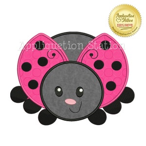 May include: A cartoon ladybug design with a smiling face, pink wings with black spots, and a gray body. The image includes the text "Appliquetion Station" and a gold seal that says "Appliquetion Station EXCLUSIVE".
