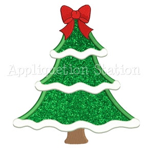 Op de afbeelding: Een groene kerstboom met een rode strik bovenop. De boom heeft witte sneeuw rond de randen van elke laag.