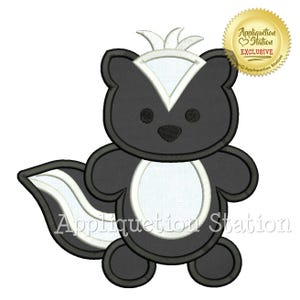 May include: A cartoon skunk applique with a black and white design. The skunk has a white stripe down its back and a white belly. The image includes the text "Appliquation Station EXCLUSIVE" in a gold seal.