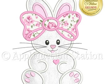 May include: A white bunny with pink ears and a pink bow with a floral pattern. The bunny is sitting with its paws in front of it. The bunny has a small pink heart on its chest. The image is a digital embroidery design.