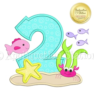 Puede incluir: Un número dos azul con lunares blancos, un pez rosa, algas verdes, una estrella de mar amarilla y un cangrejo rosa. El diseño es perfecto para una fiesta de segundo cumpleaños.