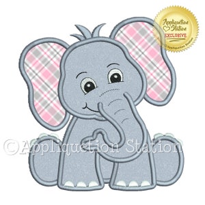 May include: A gray elephant with pink and gray plaid ears, sitting with its trunk in its mouth. The elephant has a happy expression and big eyes. The image includes the text "Appliquetion Station" in a stylized font.