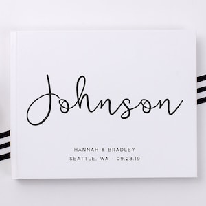 May include: White guest book with the text "Johnson" in black cursive script. Below the name is the text "Hannah & Bradley" and "Seattle, WA - 09.28.19" in black.