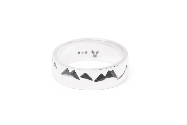 Puede incluir: Un anillo de plata con un dise&ntilde;o de cordillera grabado alrededor de la banda. El anillo est&aacute; marcado con una peque&ntilde;a "Y" en el interior.