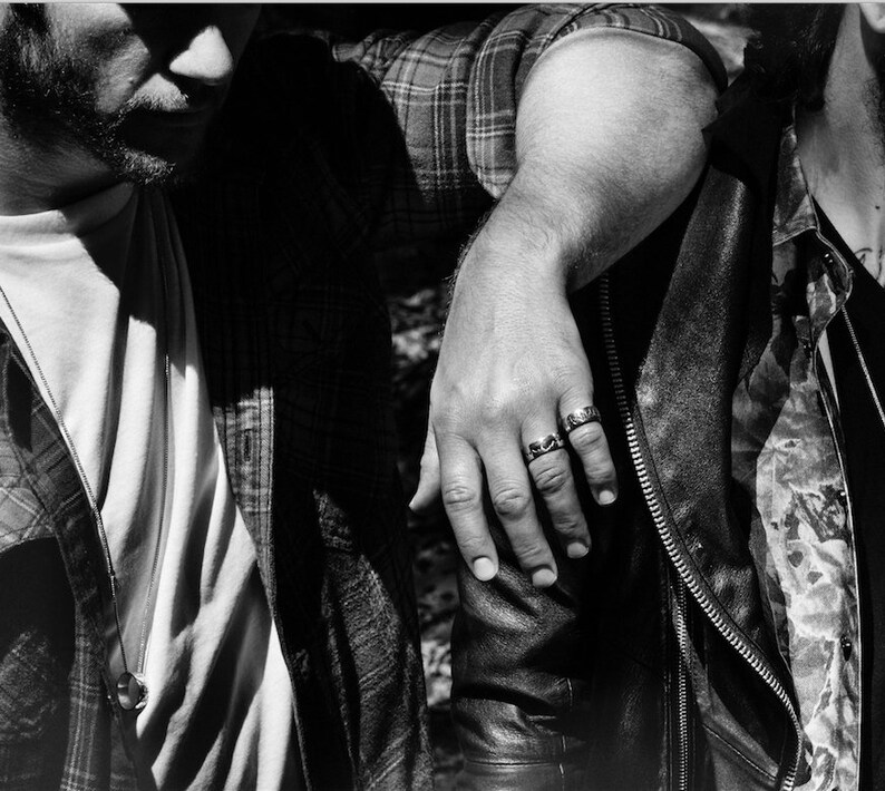Puede incluir: Dos personas de pie cerca una de la otra, una con una camisa a cuadros y la otra con una chaqueta de cuero. La persona con la camisa a cuadros tiene el brazo alrededor del hombro de la otra persona. La persona con la chaqueta de cuero lleva un anillo en el dedo.