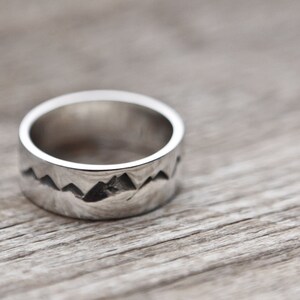 Puede incluir: Un anillo de plata con un dise&ntilde;o de cordillera. El anillo es ancho y tiene un acabado liso y pulido.