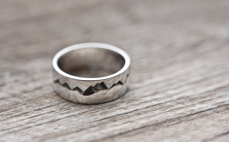 Puede incluir: Un anillo de plata con un dise&ntilde;o de cordillera. El anillo es ancho y tiene un acabado liso y pulido.