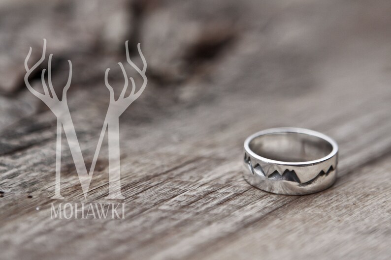 Puede incluir: Un anillo de plata con un dise&ntilde;o de cordillera. El anillo est&aacute; sobre una superficie de madera.