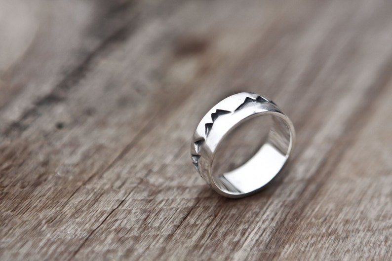Puede incluir: Un anillo de plata con una banda texturizada que presenta un dise&ntilde;o de cordillera.