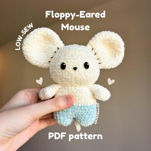 May include: A cream and light blue crocheted mouse plush toy with large floppy ears, black bead eyes, and a small black nose. The text on the image reads Floppy-Eared Mouse, LOW-SEW, and PDF pattern, with small heart icons and the handle @krompycraft.