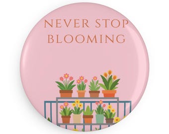 May include: A round pink pin-back button featuring the text NEVER STOP BLOOMING in orange letters. Below the text is a graphic illustration of a metal shelf holding various potted flowers in shades of pink, yellow, orange, and green.