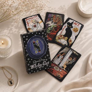 Könnte beinhalten: Ein Witchy Cat Tarotkartendeck von Dame Darcy mit einer schwarzen Schachtel, die eine Katzenillustration und Sternenmuster zeigt. Vier Karten sind abgebildet, darunter der Page der Münzen und das Ass der Münzen, mit verschiedenen Katzenmotiven.