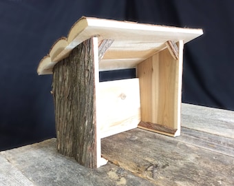 Peut inclure: Une crèche de Noël en bois avec un extérieur recouvert d'écorce et un intérieur simple et non fini. La crèche est en bois naturel et a un aspect rustique et artisanal.