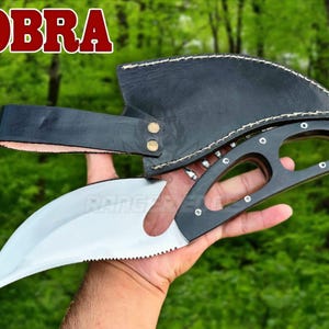 Könnte beinhalten: Ein Messer mit geschwungener silberner Klinge und schwarzem Griff, der drei Aussparungen und silberne Nieten aufweist. Das Messer enthält eine schwarze Lederscheide mit weißen Nähten und Gürtelschlaufe. Das Wort COBRA steht in rotem Text oben links.