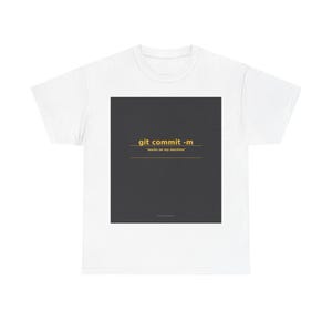 Op de afbeelding: Een wit t-shirt met korte mouwen en een gecentreerde donkergrijze vierkante afbeelding. De afbeelding toont de gele tekst "git commit -m" gevolgd door de tekst "works on my machine" in kleinere gele letters, beide onderstreept door gele lijnen.
