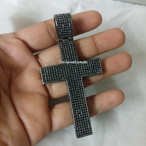 Peut inclure: Un pendentif croix en métal noir doté d'un sertissage pavé de nombreuses petites pierres noires recouvrant toute la surface avant. Le pendentif comprend une bélière rectangulaire sur le dessus et affiche le texte Crestjewelrystudio au centre.