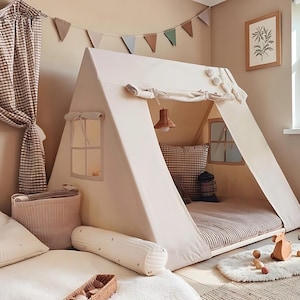 Puede incluir: Una tienda de juegos en forma de A de color crema con dos ventanas laterales con contraventanas de tela, una lámpara colgante en el interior y una alfombrilla acolchada. La estructura es de lona e incluye una apertura frontal enrollable.