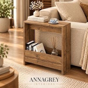 May include: A rectangular wooden side table with a medium brown wood grain finish. The table features a flat top surface and a lower storage compartment designed for holding books and magazines, with an open frame construction and side panels.