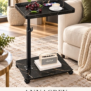 May include: A black marble-patterned side table with a height-adjustable metal post and four caster wheels. The table features a rectangular top surface and a matching base, with a small bowl of cherries, a smartphone, and a coffee cup on top.