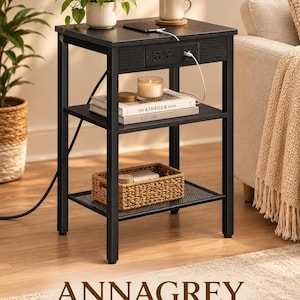 May include: A black wooden side table with a metal frame, featuring a top surface with a built-in power strip containing two electrical outlets and two USB ports. The table includes a middle shelf and a bottom mesh shelf, with a power cord extending.