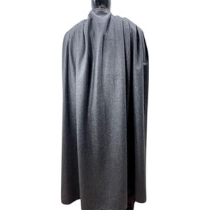 May include: A floor-length, dark gray cape featuring a high collar and a structured, pleated design. The garment is crafted from a solid-colored, textured fabric that drapes vertically from the shoulders, creating a full and flowing silhouette.