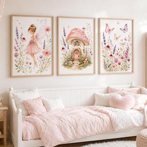 May include: A set of three framed wall art prints featuring watercolour illustrations. The left print shows a fairy in a pink dress, the centre print depicts a mushroom house, and the right print displays butterflies and wildflowers in shades of pink and purple.