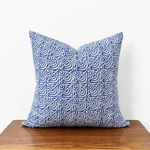 May include: A square throw pillow featuring a repeating grid pattern of blue hand-drawn style fan shapes on a light gray background. The fabric has a visible texture and the design consists of alternating triangular segments within each square block.