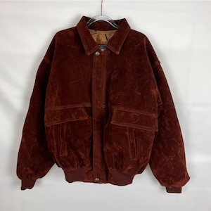Peut inclure: Un blouson aviateur en daim marron foncé doté d'un col classique, d'une fermeture à boutons métalliques sur le devant, de deux grandes poches à rabat sur la poitrine, ainsi que de poignets et d'un ourlet en tricot côtelé. Doublure beige avec logo V.
