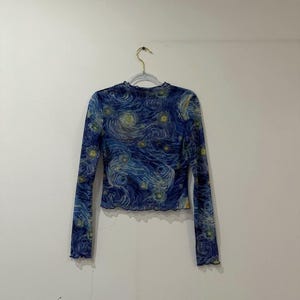 Könnte beinhalten: Ein langärmeliges Netzoberteil mit einem blauen und gelben Wirbelmuster, das an Sternennacht erinnert. Das Kleidungsstück hat einen Rundhalsausschnitt und einen gewellten Saum an den Ärmelbündchen sowie am unteren Abschluss.