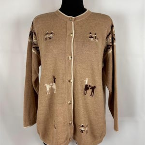 May include: A tan long-sleeve knit cardigan featuring a crew neckline and a front button closure. The garment is decorated with small, dark brown and white intarsia patterns of llamas and figures, along with geometric designs on the shoulders.