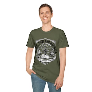 May include: An olive green short-sleeve t-shirt featuring a graphic print of a shield containing a cross, a barbell, and an open book. The text reads BIBLE, BOW AND BARBELL and FAITH, HUNTING, FITNESS. The design is rendered in shades of white and grey.