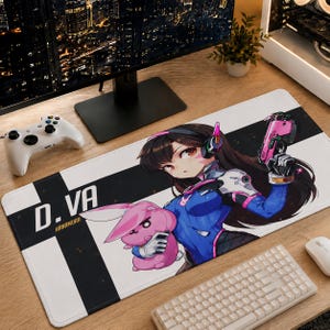 May include: A rectangular desk mat featuring an anime-style illustration of the character D.Va from Overwatch. The design includes the text D.VA and HANAMURA, a pink rabbit character, and the character holding a pink pistol on a black and white background.