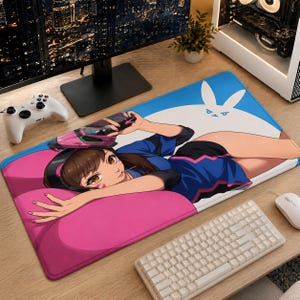 May include: A rectangular desk mat featuring a colorful anime-style illustration of a character with brown hair and headphones, wearing a blue and black outfit. The character holds a pink and black futuristic blaster against a blue and pink background.