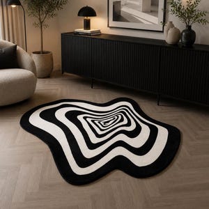 May include: An irregular, organic-shaped area rug featuring a high-contrast black and white pattern of concentric, wavy lines that create a swirling, optical illusion effect across the entire surface of the floor covering.