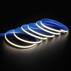 May include: A flexible LED strip light coiled into several overlapping loops. The strip features a bright white light-emitting surface on one side and a solid blue backing material, creating a high-contrast appearance against the dark background.