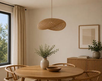 Op de afbeelding: Een gevlochten rotan hanglamp met een organische, asymmetrische vorm die aan een dun snoer aan het plafond hangt, met een natuurlijke lichtbruine afwerking en een complexe, verweven textuur die een zacht, diffuus lichteffect creëert.
