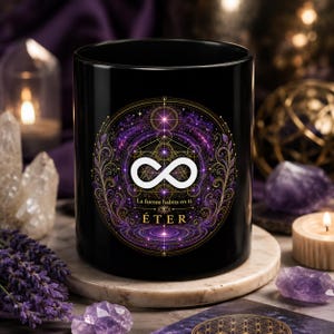 May include: A black cylindrical mug featuring a central circular graphic with a white infinity symbol, intricate gold geometric patterns, and purple nebula-like swirls. The text reads "La fuente habita en ti." and "ÉTER" in gold lettering.
