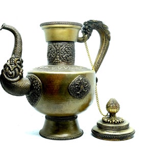 May include: A gold-colored metal teapot with a dragon-shaped spout and handle. The teapot has intricate carvings and a chain attached to the lid.