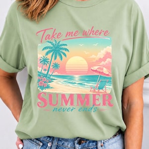 May include: A sage green t-shirt featuring a graphic print of a beach scene at sunset with palm trees, a beach chair, and an umbrella. The text reads "Take me where SUMMER never ends" in pink and teal lettering across the center of the shirt.