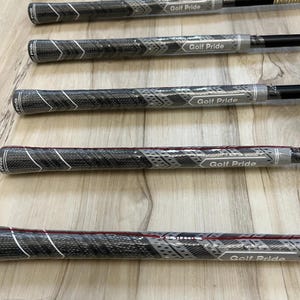 Puede incluir: Una colecci&oacute;n de empu&ntilde;aduras para palos de golf con un patr&oacute;n texturizado en negro y gris con detalles en blanco en forma de chevr&oacute;n. Cada empu&ntilde;adura est&aacute; envuelta en pl&aacute;stico protector transparente y muestra el logotipo de Golf Pride en blanco.