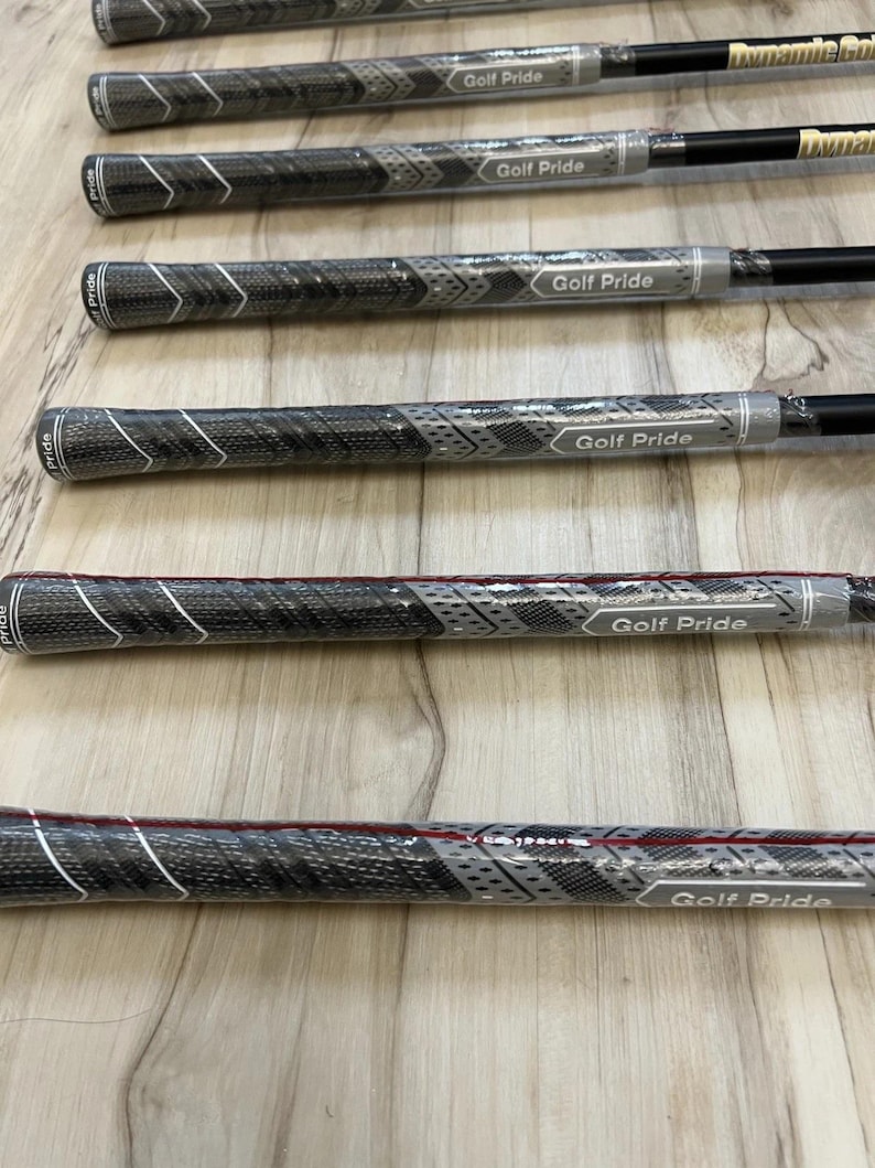 Puede incluir: Una colecci&oacute;n de empu&ntilde;aduras para palos de golf con un patr&oacute;n texturizado en negro y gris con detalles en blanco en forma de chevr&oacute;n. Cada empu&ntilde;adura est&aacute; envuelta en pl&aacute;stico protector transparente y muestra el logotipo de Golf Pride en blanco.