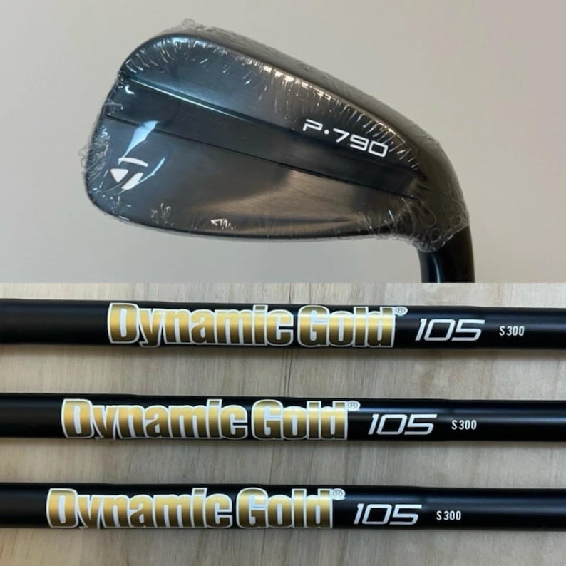 Puede incluir: Una cabeza de palo de golf TaylorMade P.790 negra envuelta en pl&aacute;stico transparente, colocada sobre tres varas de palo de golf negras. Cada vara presenta el texto Dynamic Gold 105 S300 en dorado y blanco impreso claramente a lo largo.
