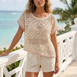 May include: A beige crochet top with a round neckline and short sleeves, featuring an intricate openwork pattern and a subtle pink trim along the edges, paired with beige linen shorts that have two front pockets and a button closure.